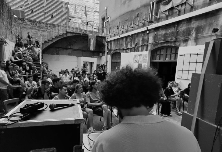 Black and white photo of an audience of people in the old building of the Massana in Barcelona with a guy with curly hair in the front